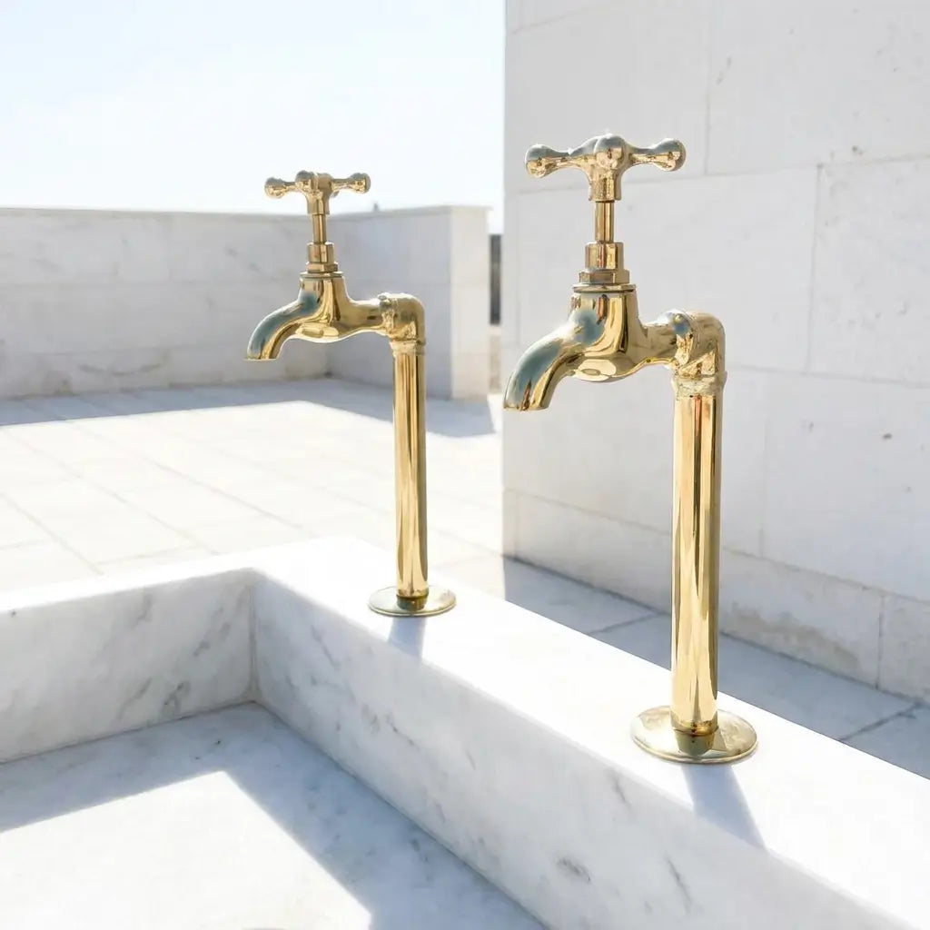 Two elegant brass water filter faucets with cross handles installed on a luxury white marble structure in a bright outdoor setting.