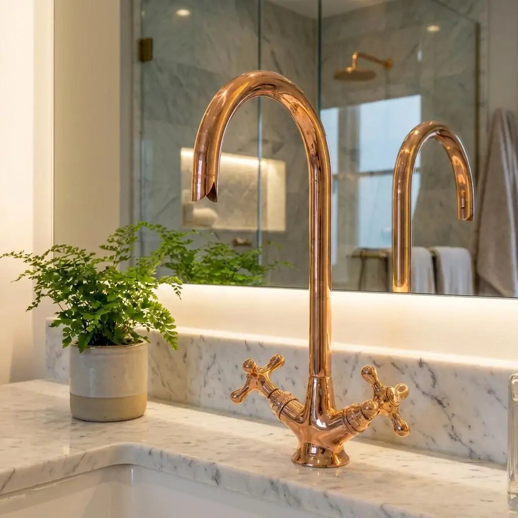 Polished copper gooseneck faucet with dual cross handles on a white marble vanity top in front of a large bathroom mirror.