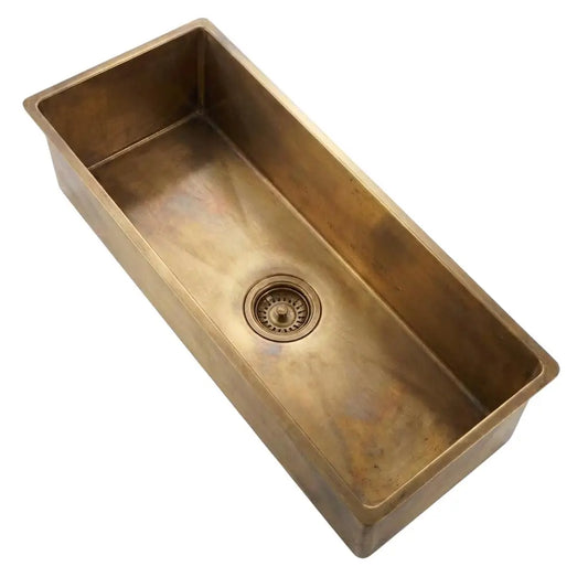 Angled top view of a rectangular brass kitchen sink basin showing the center drain on a white background