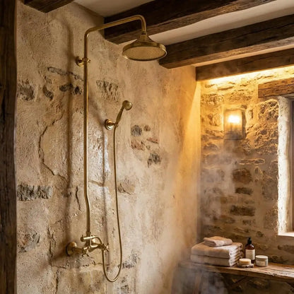 Rustic unlacquered brass shower system with a Moroccan wall-mounted rain head on an earthy textured tadelakt plaster wall with exposed wooden ceiling beams.