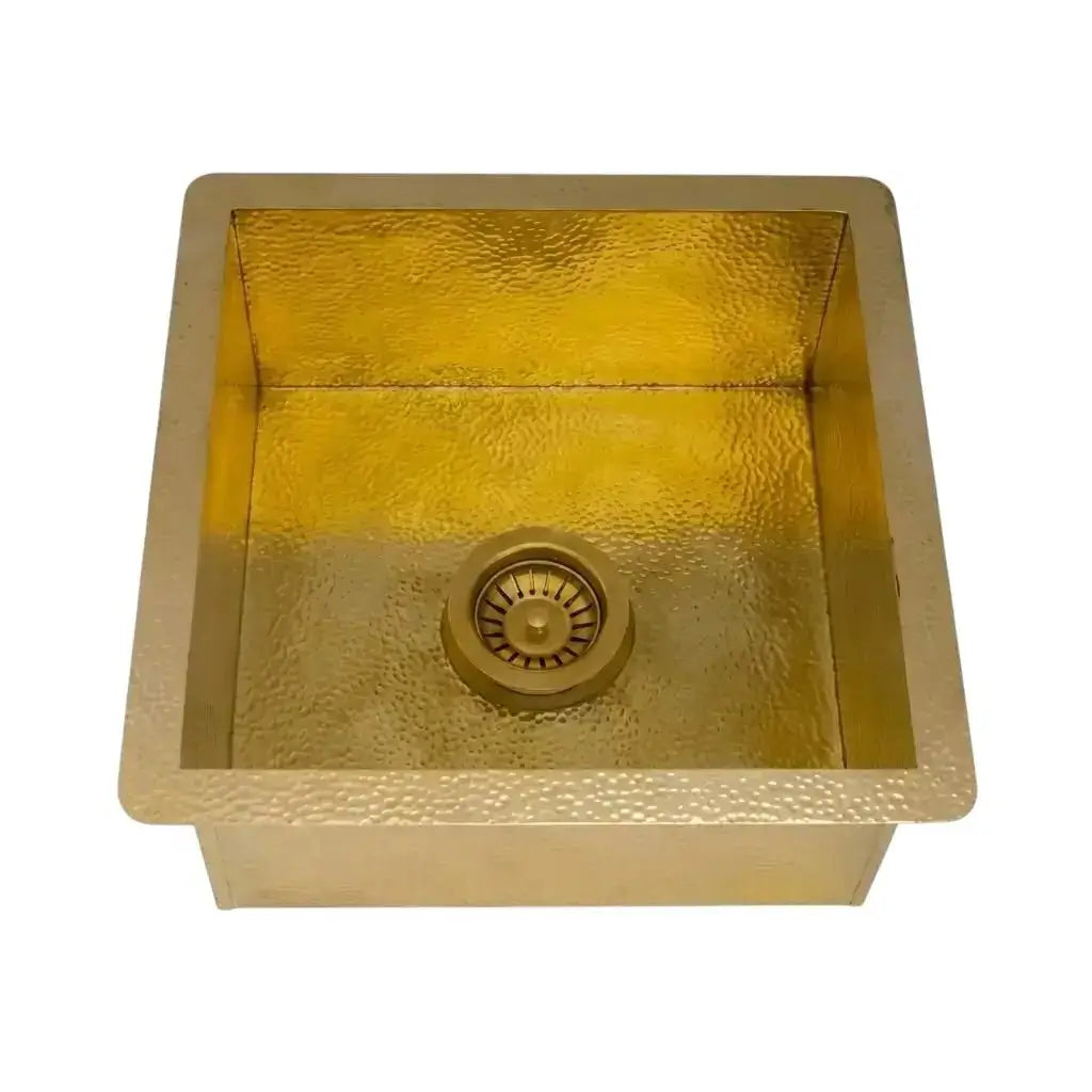 Isolated square hammered brass kitchen sink with integrated drain assembly displayed on a clean solid white studio background.