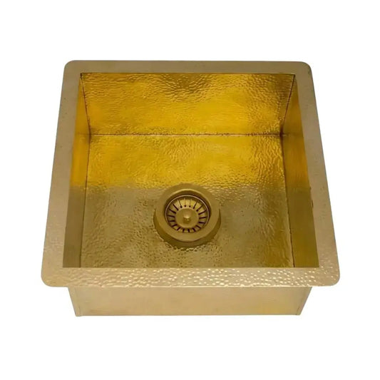 Isolated square hammered brass kitchen sink with integrated drain assembly displayed on a clean solid white studio background.