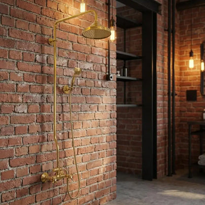 Unlacquered brass exposed pipe shower system with a large round rainfall head and handheld sprayer mounted on an industrial red brick wall in a loft bathroom.