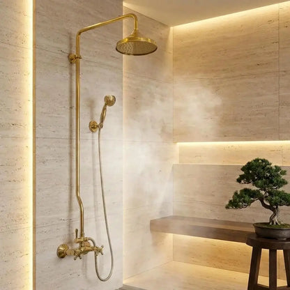Unlacquered brass exposed pipe shower system with rainfall head and handheld sprayer set against luxury marble tiles.