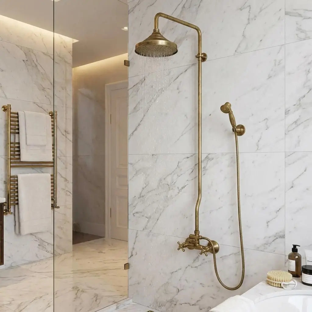 Side angle view of an unlacquered brass shower system with a Moroccan wall-mounted rain head and handheld sprayer on white marble tiles.