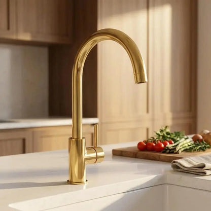 Close up back view of an unlacquered brass curved sink faucet on a white kitchen countertop.