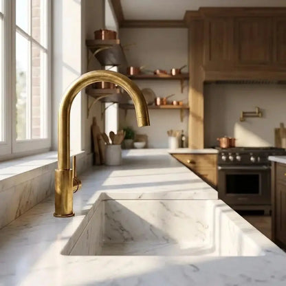 Perspective view of an unlacquered brass curved faucet in a rustic kitchen with wooden shelves and copper pots.