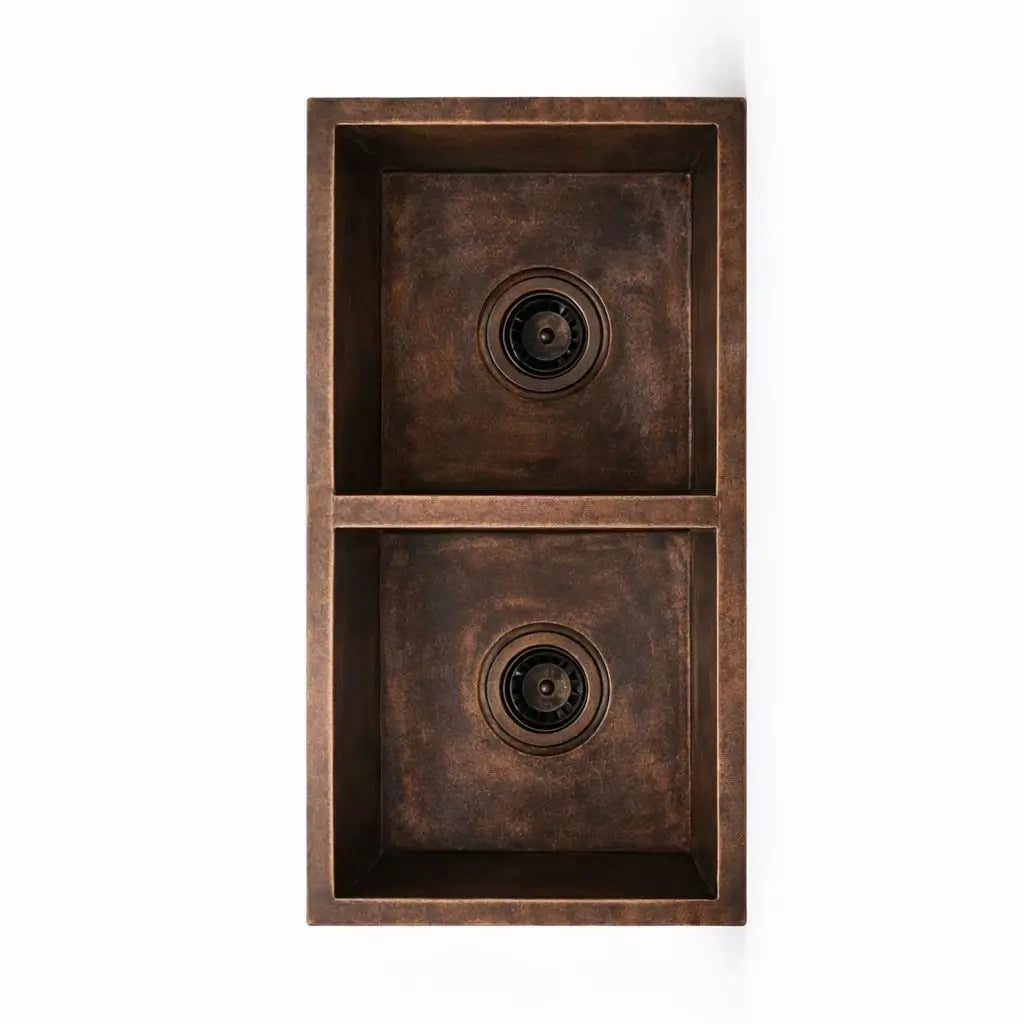 Vertical overhead view of handmade rustic copper double bowl kitchen sink on a plain background