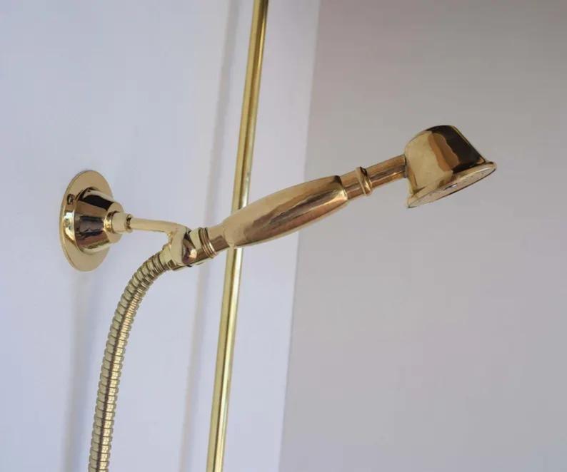 Close-up of an unlacquered brass handheld shower sprayer with sleek design and flexible hose.